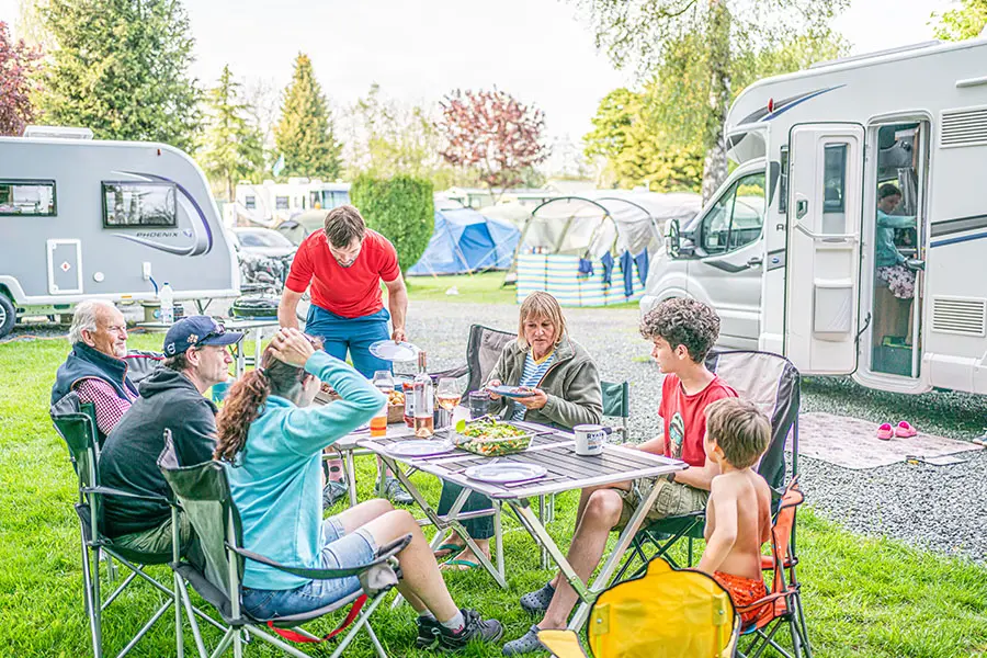 Family eating around table outside Bailey motorhome