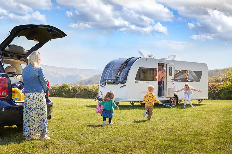 Grandchildren running from their car towards grandmother outside her caravan