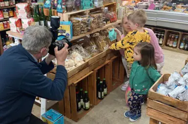 Photographer taking photos of children and their grandmother shopping in a farm shop