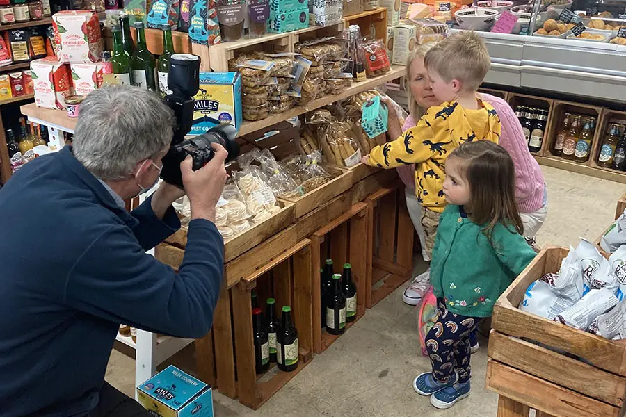 Photographer taking photos of children and their grandmother shopping in a farm shop