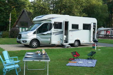 A Bailey of Bristol Adamo motorhome on a pitch in front of an outside table and chairs set-up for food.