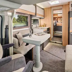 Spacious motorhome living area – A bright and inviting motorhome interior with a well-designed lounge and dining area. Features include plush seating, a compact yet functional kitchen, and a comfortable layout leading to a bedroom at the rear.