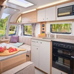 Bright and airy interior of the Bailey Phoenix GT75 caravan, featuring a kitchen area with oven, microwave, sink, and cozy lounge seating.