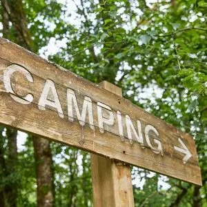 A rustic wooden sign pointing towards a campsite, set against a lush green forest background, capturing the adventurous spirit of outdoor exploration.