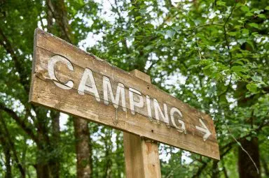 A rustic wooden sign pointing towards a campsite, set against a lush green forest background, capturing the adventurous spirit of outdoor exploration.