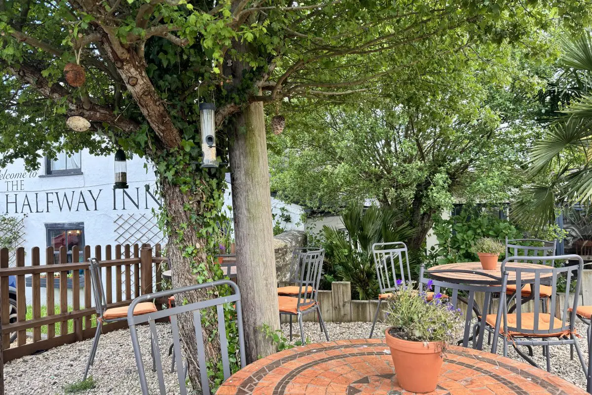 Outdoor seating area at The Halfway Inn with garden tables, trees and the pub building in the background.