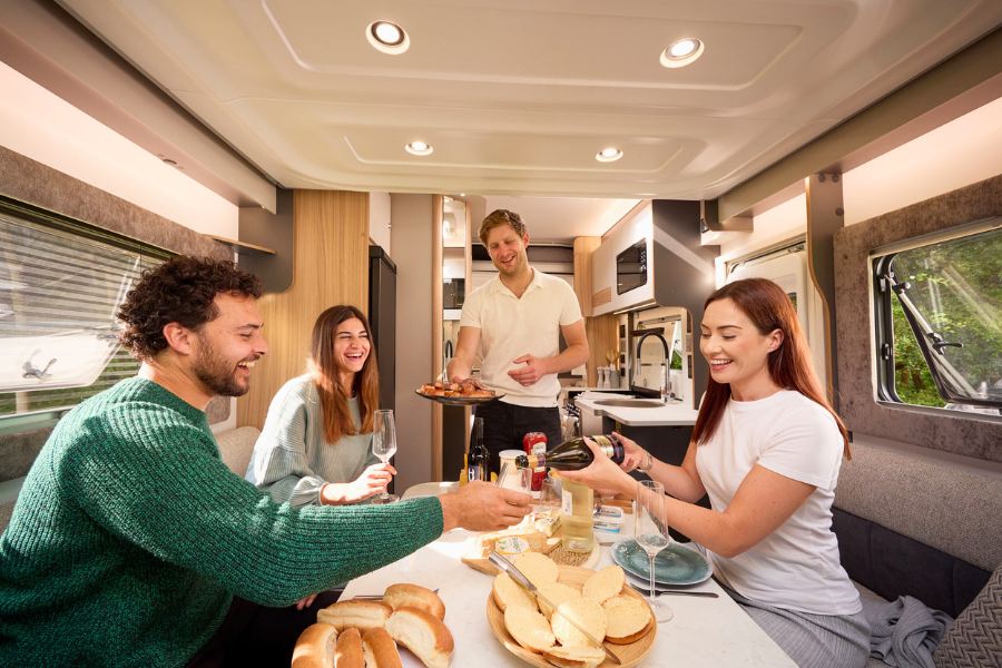 Group of friends enjoying a meal and drinks in the Bailey Adamo 75-4DL motorhome, showcasing sociable dining layout and contemporary design.