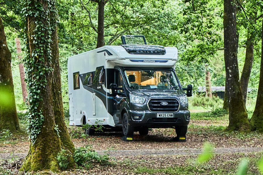 A Bailey Adamo motorhome parked among tall trees at Huttopia Lac de Sillé, blending into a peaceful woodland camping pitch.