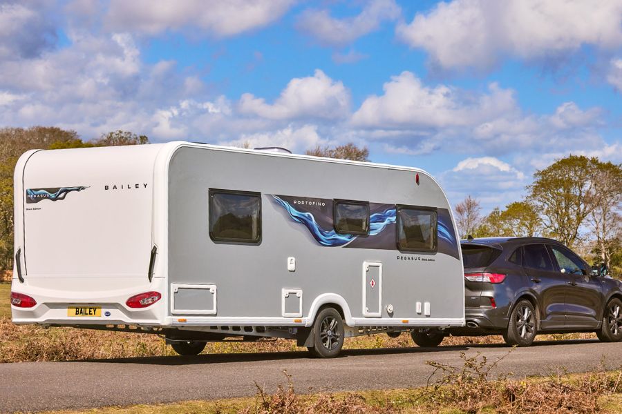 Rear and side view of the Pegasus Black Edition Portofino caravan being towed, with sleek cobalt and black graphics, showcasing the new exterior design.