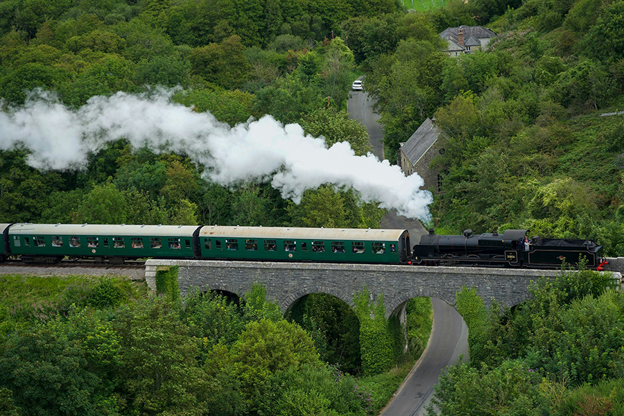 A steam train pushing carriages over a bridge. Photo by Nick Fewings on Unsplash