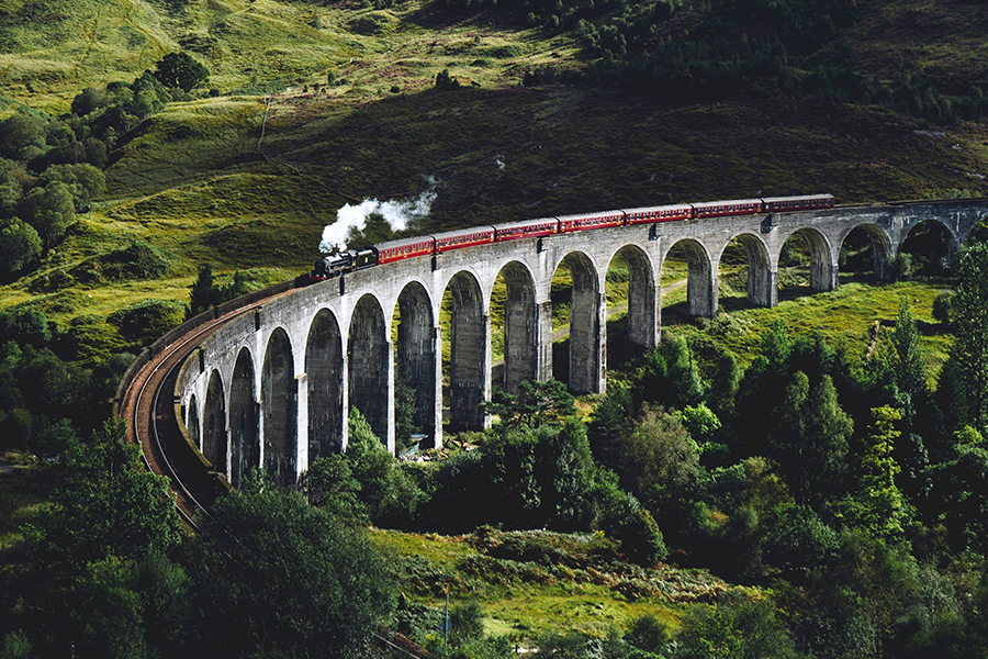 The famous Glenfinnan viaduct seen from above with a steam train going over it. Photo by Jack Anstey on Unsplash